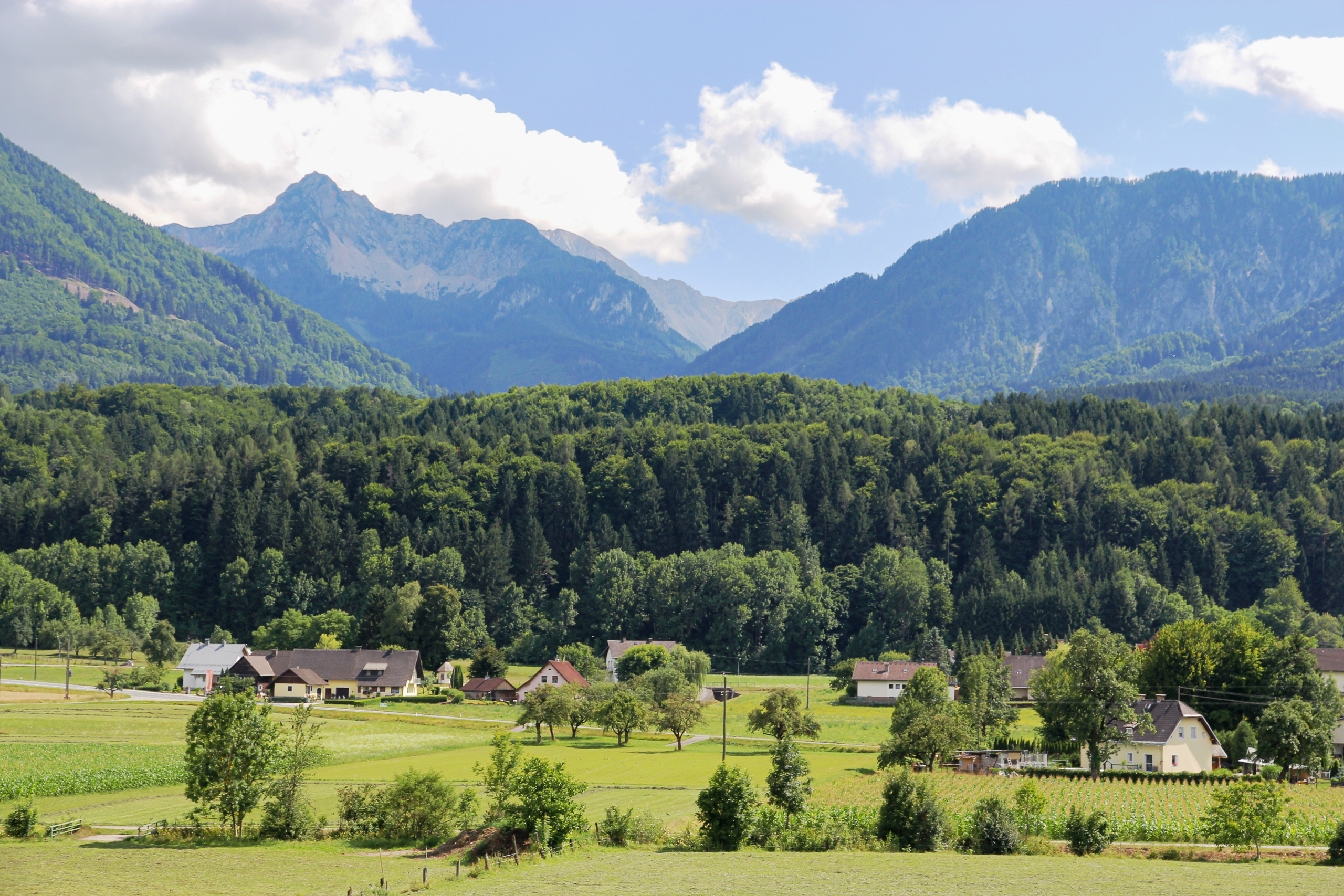 Höfe und Wiesen im weiten Tal, dahinter die ersten schroffen Gipfel
